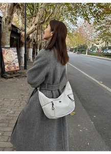 Détail d'un sac bandoulière croissant en cuir crème porté sur un manteau gris en laine