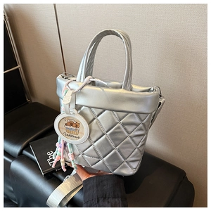 Detail of silver quilted bucket bag with woven wide strap and cute capybara charm accessory