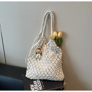 Detail of white macrame woven tote bag with cartoon doll pendant and yellow tulips