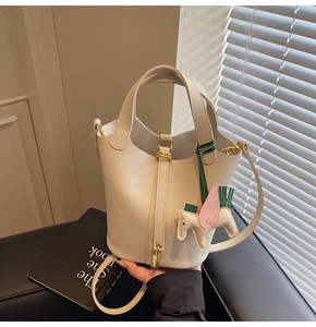 Detailed view of beige pebble leather bucket bag with horse charm on black leather chair