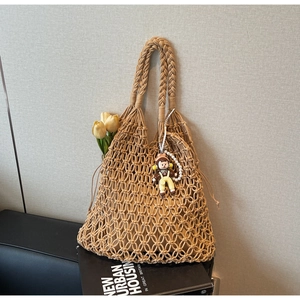 Detail of hand-woven hollow tote bag featuring braided handles and cartoon doll pendant