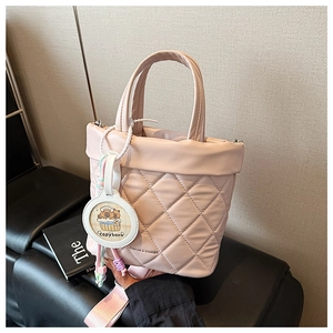 Close-up of pink quilted bucket bag with Capybara charm and branding on black bench