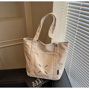 Close-up of beige canvas tote bag with contrast blue stitch detail and outer pocket