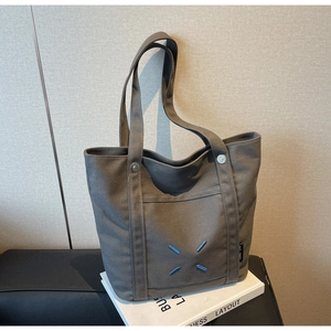 Detail of dark grey canvas tote bag featuring blue X-shaped stitching and side woven label
