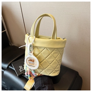 Detail shot of quilted lemon yellow bucket bag with capybara charm and wide shoulder strap