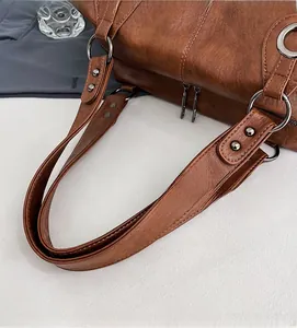 Detailed close-up of brown textured leather tote bag showing metal ring and rivet accents