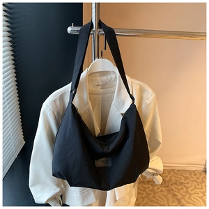 Detail of a large black nylon hobo bag with adjustable wide strap on a white suit jacket