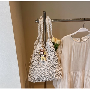 Detail of hand-woven hollow knit tote bag in cream white with a cute doll charm hanging