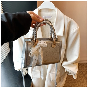 Detail of silver metallic handbag featuring woven handle and white lace bow accessory