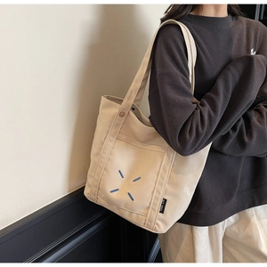 Detail of off-white canvas tote bag featuring front pocket with blue X-stitch embroidery