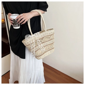 Detail of hand-woven straw tote bag featuring elegant white lace bows and fringe accents