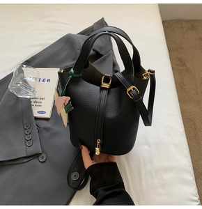 Detail view of black lychee grain bucket bag with gold padlock and leaf pendant charm