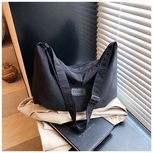 Detail of black nylon shoulder bag with TZIMEI logo placed on a light blazer and book