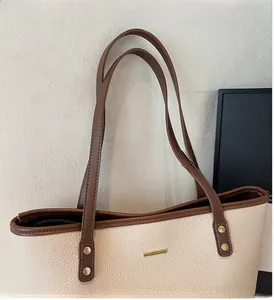 Dettaglio della borsa tote in pelle beige con manici marroni e rivetti dorati