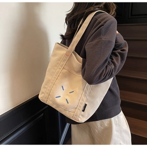 Detail shot of canvas tote bag showing side brand tag and minimalist blue stitching