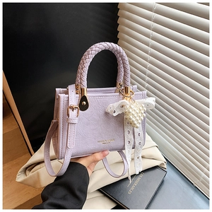 Detail of purple lychee leather square bag with woven handle and pearl heart charm