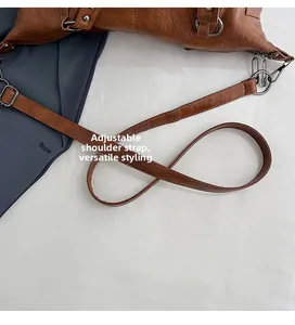 Detail view of the adjustable shoulder strap and silver metal buckle on brown leather bag