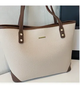 Dettaglio della borsa tote opaca bianco sporco con finiture in pelle marrone e logo oro