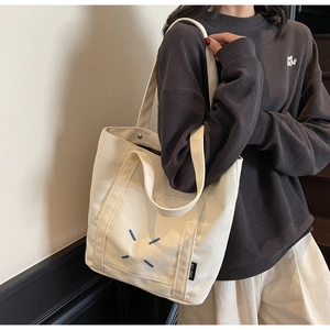 Detail of off-white canvas tote bag featuring blue cross stitching and a magnetic buckle
