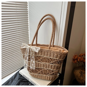 Close-up of a woven straw tote bag featuring elegant lace bow detail and circular handles