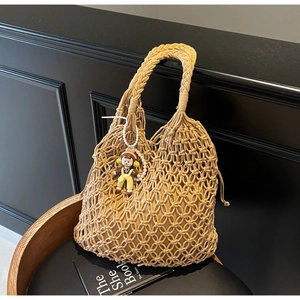 Detail of hollow woven tote bag featuring thick braided handles and pearl doll charm