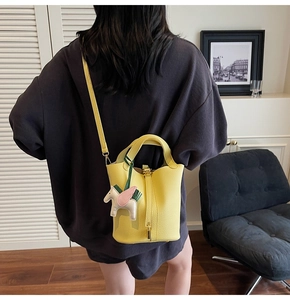 Detail of yellow pebbled leather bucket bag featuring a colorful horse charm on the handle