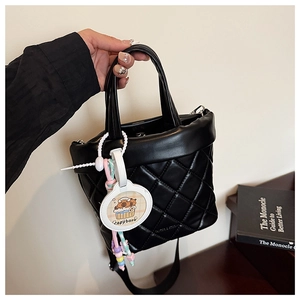 Detail of black quilted leather bucket bag with a cartoon capybara charm and wide strap