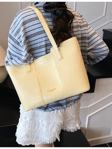Minimalist beige crocodile embossed tote bag with gold lettering shown on model shoulder
