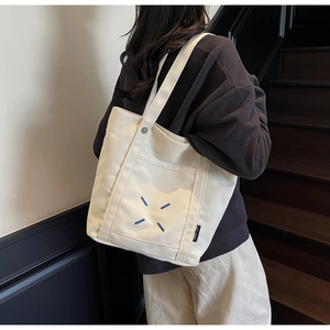 Detail of white canvas tote bag featuring blue X-shaped embroidery and a minimal woven label