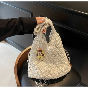 Detail of white hollow woven tote bag with cotton rope craft and cute doll charm accessory