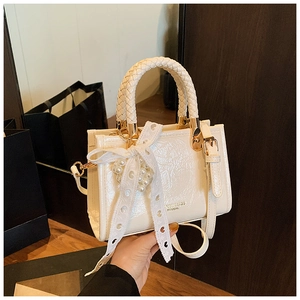 Detail of cream-white handbag featuring woven handle and pearl lace bow accessory