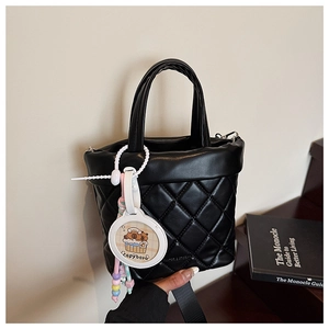 Close-up of black quilted bucket bag featuring a cute Capybara charm and wide strap