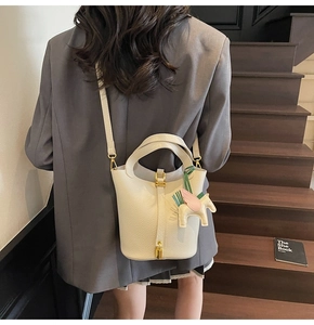Close-up of beige litchi grain bucket bag with gold lock and winged horse pendant