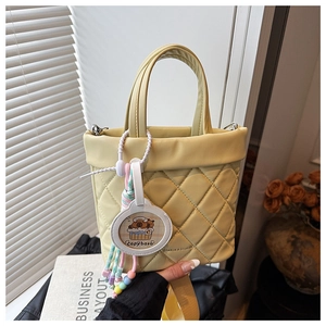 Detail of yellow quilted bucket bag featuring a cute capybara charm and wide strap