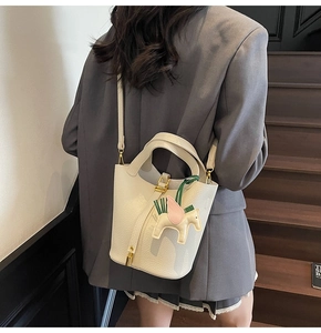 Detail of white litchi leather bucket bag with gold lock and yellow pony charm on strap