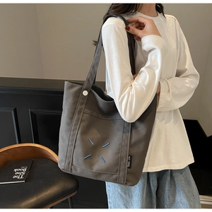 Detail of dark gray canvas tote bag featuring blue cross embroidery and magnetic button