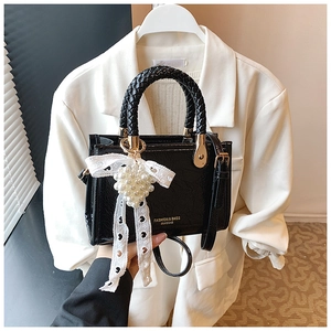 Detail of black patent leather crossbody bag with pearl cluster and lace bow charm