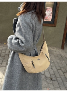 Détail du sac bandoulière beige en demi-lune avec doubles zips sur manteau gris