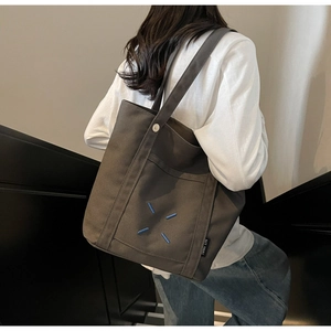 Rear view of model carrying a dark coffee canvas tote bag with blue cross stitching