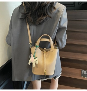 Litchi texture khaki bucket bag with horse charm and adjustable strap worn by model