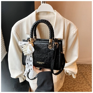 Close-up of black glossy crossbody bag with woven handle and elegant pearl lace charm