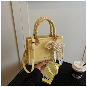 Macro detail of yellow pleated leather bag with pearl bow charm and braided handle
