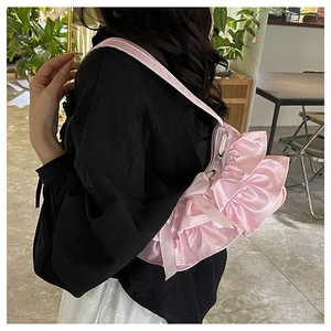 Detailed view of pink ruffled satin handbag on model in a cozy indoor cafe setting