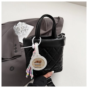 Close-up of quilted black leather bucket bag with a cute Capybara charm and wide strap