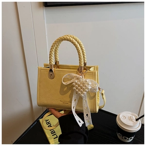 Close-up of yellow leather handbag featuring braided handle and pearl heart charm