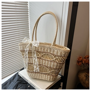 Detail of woven straw tote bag featuring white lace bow and round braided handle
