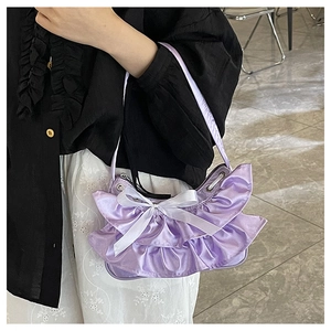 Detail of purple satin handbag featuring ruffled edges and white silk ribbon bow accent