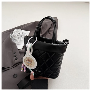 Detail of black quilted bucket bag featuring a cute capybara pendant and wide shoulder strap