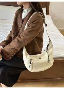 Détail d'un sac bandoulière demi-lune beige avec doubles fermetures éclair et sangle réglable