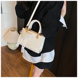 Detail of cream crossbody bag with woven handle and pearl heart charm accessory